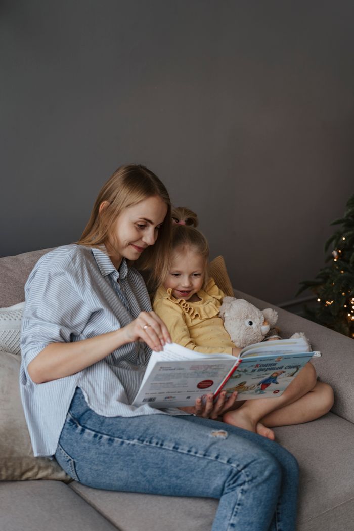 Warm and cozy moment of a mother and daughter reading a book on the sofa.
